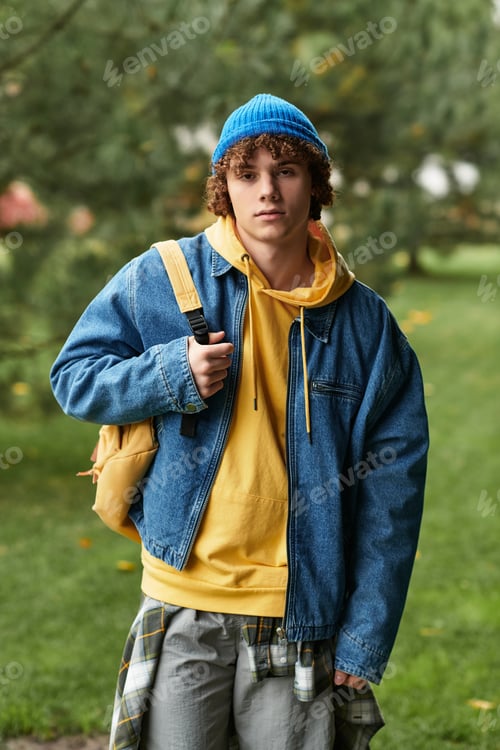 Preview: Curly teenager in a blue beanie enjoys an autumn day outdoors in casual attire