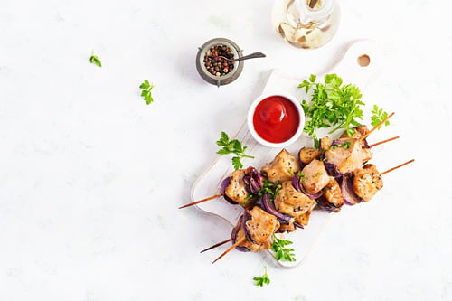 Preview: Grilled chicken kebab with red onions on a light table.