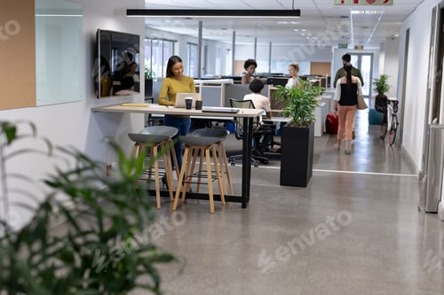 Preview: African american businesswoman using laptop against colleagues working at modern workplace