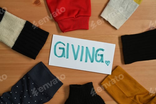 Preview: GIVING label surrounded by old warm clothes on wooden table.