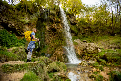 Preview: Young hiker stopped beside a mountain waterfall to rest
