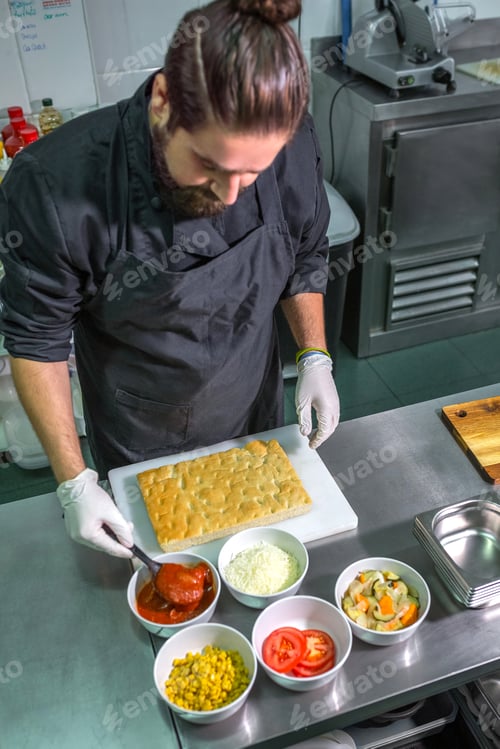 Preview: Professional male chef preparing pizza with fresh ingredients in commercial kitchen