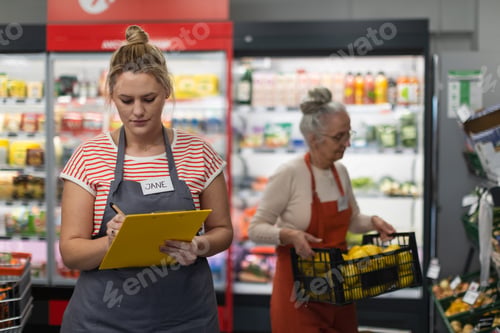 Preview: Young shop assistant in supermarket in vegetable shell, in bakcground is her colleague filling stock