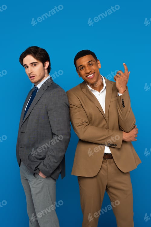 Preview: Elegant interracial men in suits standing confidently isolated on blue