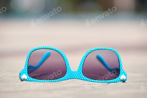 Preview: Closeup of blue sunglasses on swimming pool side on warm sunny day. Summer vacation concept.