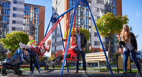 Preview: Happy family - father, mother and children having fun together on playground.