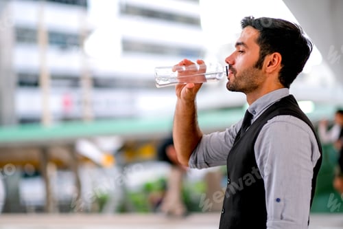 Preview: White business handsome man drink water from bottle during day time in the city for refreshment.