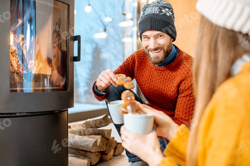 Preview: Couple with hot drinks near the fireplace during winter time