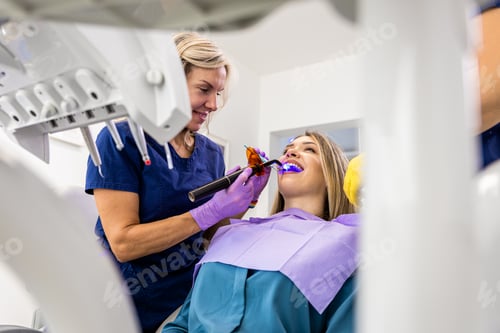 Preview: Female dentist with assistant working in dental clinic examining patient teeth.