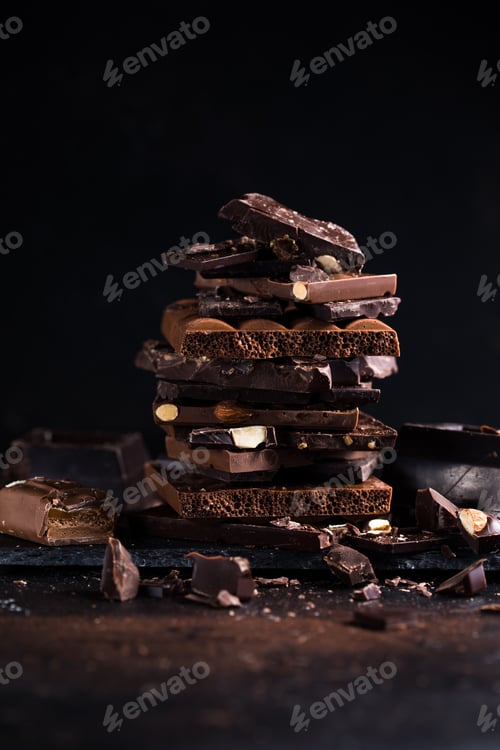 Preview: Bar of Chocolate tower pieces. Hazelnut chunks of broken chocolate. Sweet food photo concept.