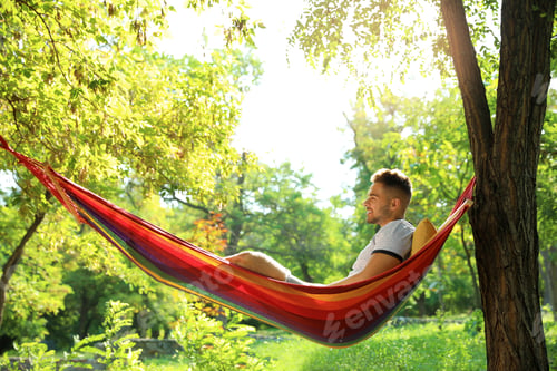 Preview: Young man resting in comfortable hammock at green garden