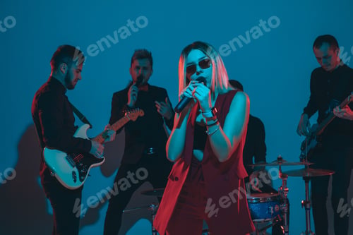 Preview: Young caucasian musicians, band performing in neon light on blue studio background, singer in front