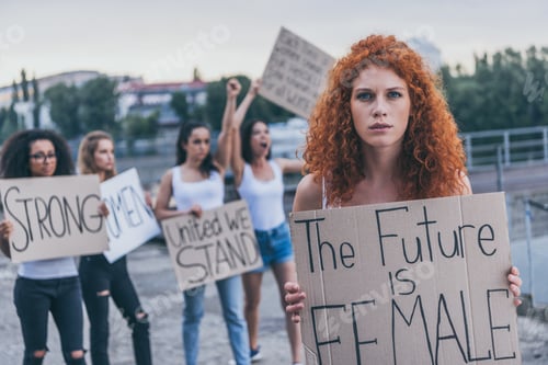 Preview: selective focus of redhead girl holding placard with future is female letters near multicultural