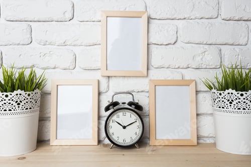 Preview: Decorative table setup with empty frames and a clock on a wooden surface near brick wall