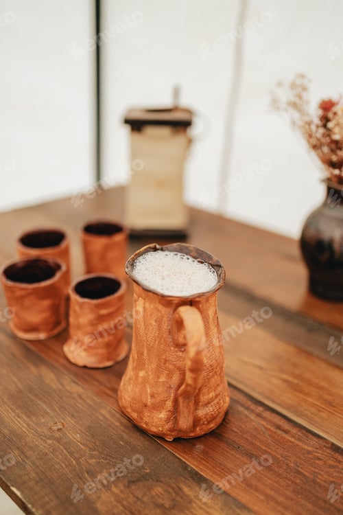 Preview: Vertical closeup shot of handmade pottery cups with one full of mead beer on a wooden table