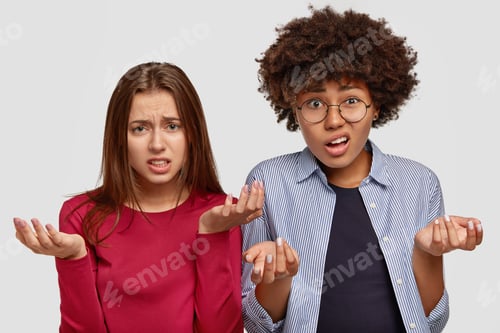 Preview: Photo of clueless two young multiethnic women with uncertain displeased looks, frown faces, spread p