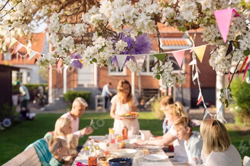 Preview: Friends with children (4-5, 8-9, 12-13) sitting at picnic table in garden