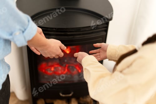 Preview: Couple warming hands by the fireplace at home