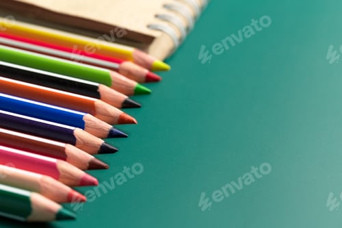 Preview: Colorful pencils lined up next to a blank notebook on a green surface