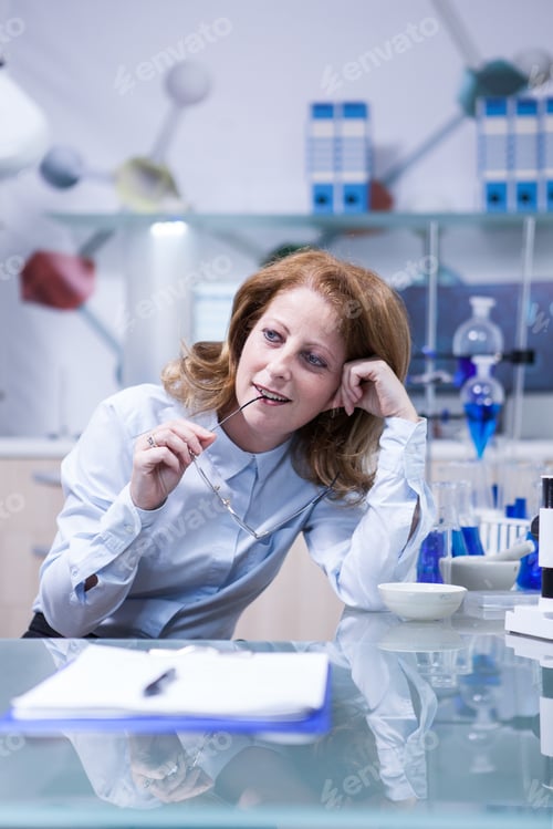 Preview: Portrait of middle age woman playing with her glasses while sitting at her office in laboratory