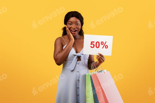 Preview: Good shopping, huge discounts. Happy young black woman holding gift bags, showing SALE sign, excited
