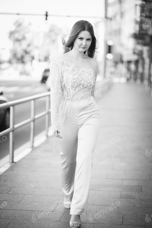 Preview: Vertical grayscale shot of a beautiful young Caucasian female posing outdoors in an elegant jumpsuit