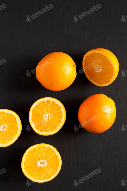 Preview: Halved and whole oranges on a black background, top view. Overhead, from above, flat lay.