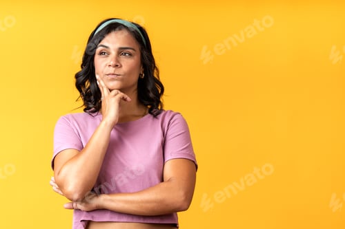Preview: Pensive woman reflecting with hand on chin against yellow background