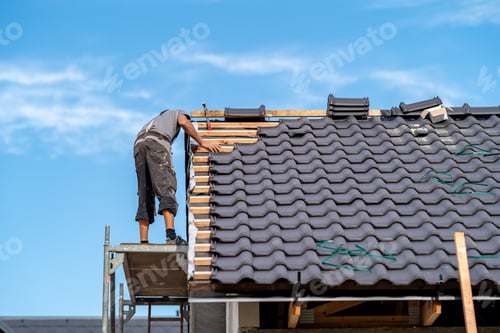 Preview: builder on the roof of a family house, building a roof covering from ceramic tiles