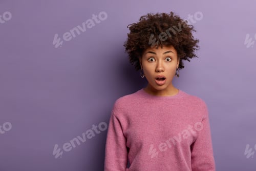 Preview: Horizontal shot of embarrassed curly young woman gasps from wonder, opens mouth in wow sound, hears