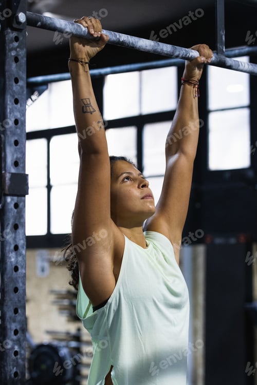 Preview: Focused ethnic woman exercising on crossbar in gym