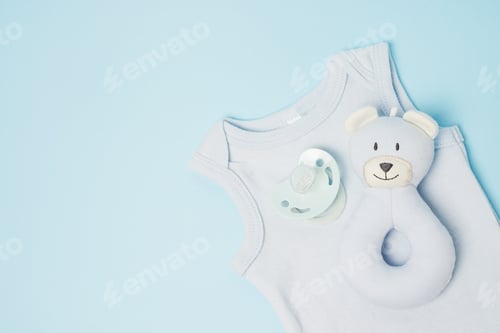 Preview: Clothes, toy and pacifier for newborn boy on blue table with copy space. Baby background
