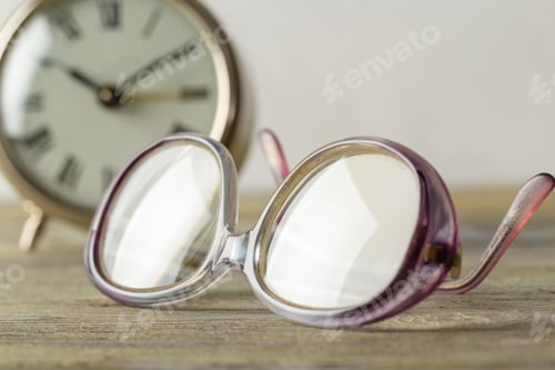 Preview: Old clock and clear glasses on a wooden table near a wall in a living space