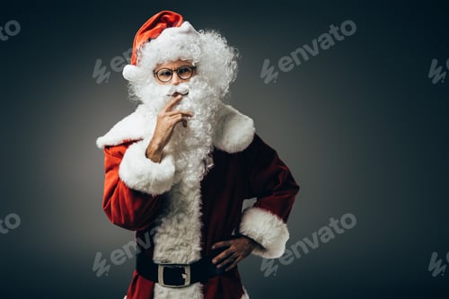 Preview: thoughtful santa claus in costume holding hand near mouth isolated on grey background