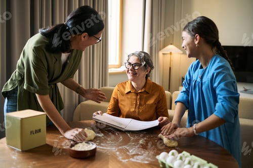 Preview: Senior Woman Guiding Family Baking Together at Home
