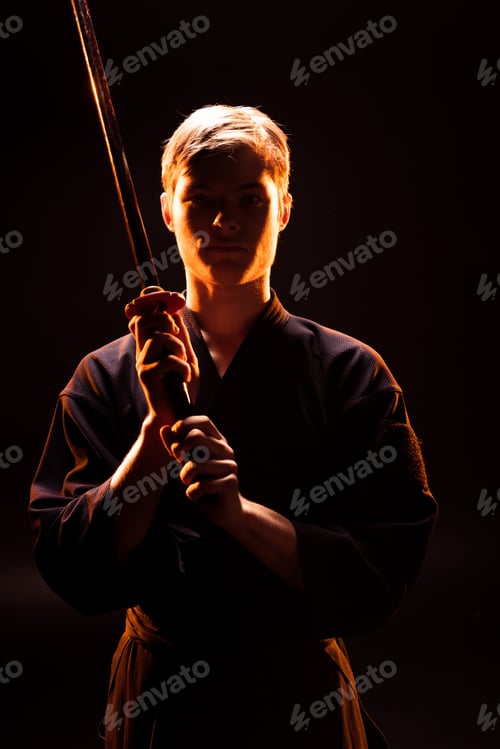 Preview: Young man in kimono holding kendo sword on black