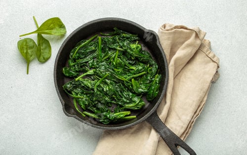 Preview: Healthy steamed spinach leaves in cast iron pan on white background top view