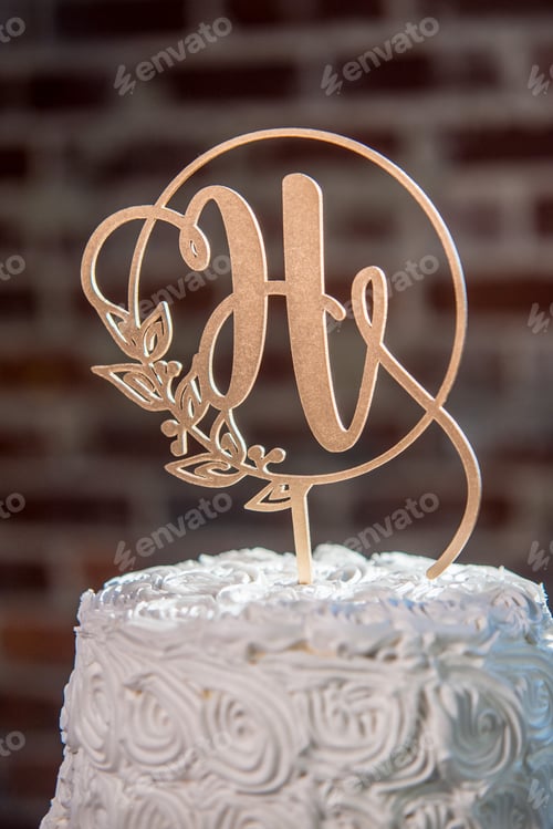 Preview: Vertical closeup shot of a H-shaped topping on a beautiful white wedding cake