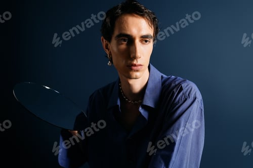 Preview: Stylish man poses elegantly with a reflective surface against a rich blue backdrop