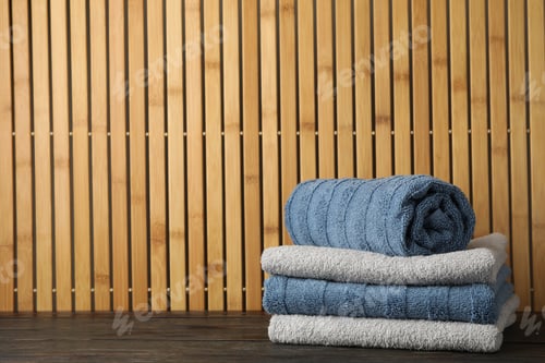 Preview: Folded towels on wooden table against bamboo background, space for text