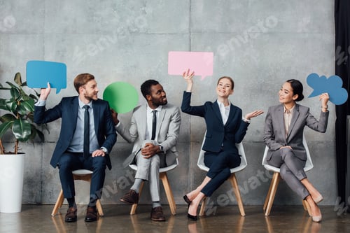 Preview: smiling multiethnic businesspeople holding speech bubbles and thought bubble while sitting in