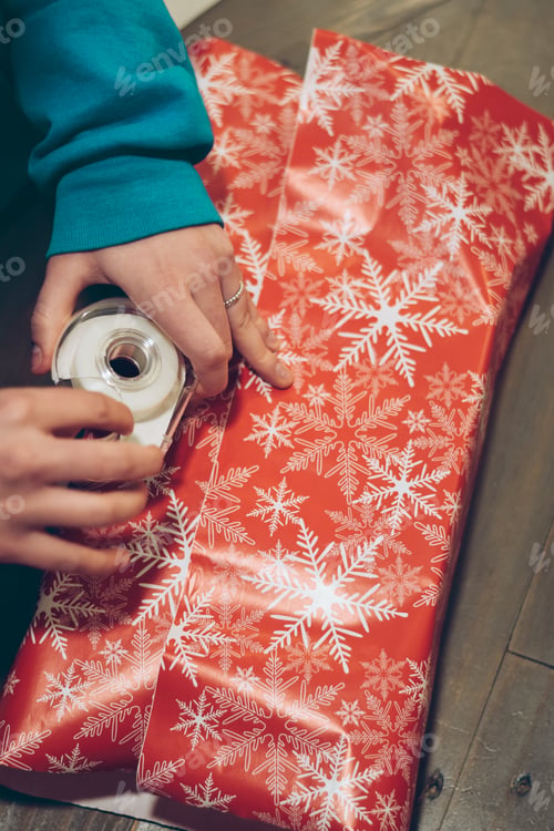 Preview: Hands of young woman using tape to wrap Christmas presents