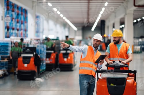 Preview: Warehouse manager guiding worker driving forklift with digital tablet