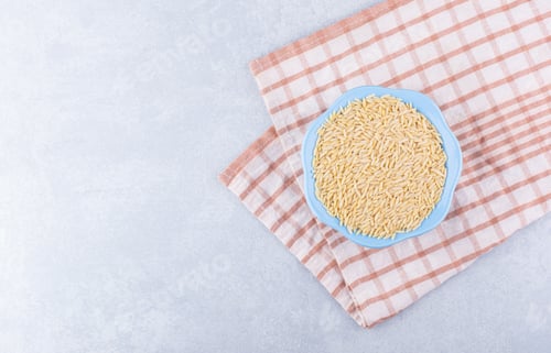 Preview: Blue bowl full of brown rice placed on a folded tablecloth on marble background