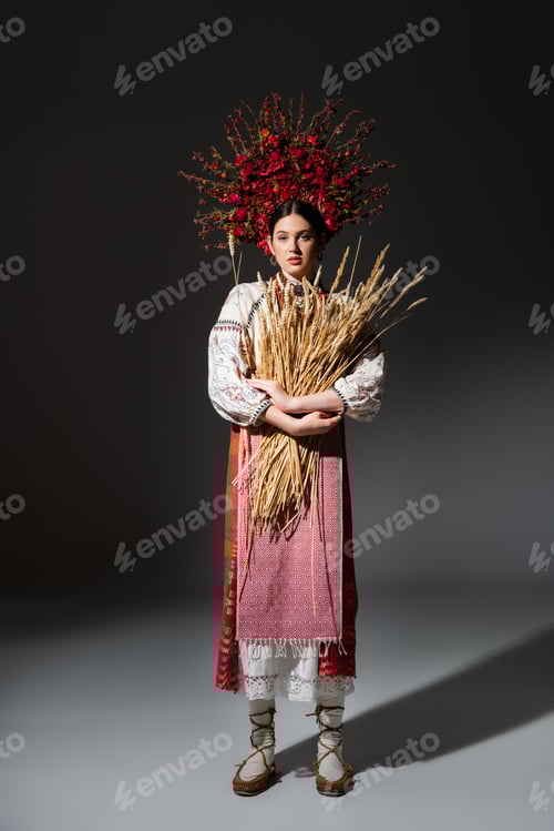 Preview: full length of brunette ukrainan woman in red wreath with berries holding wheat spikelets on black