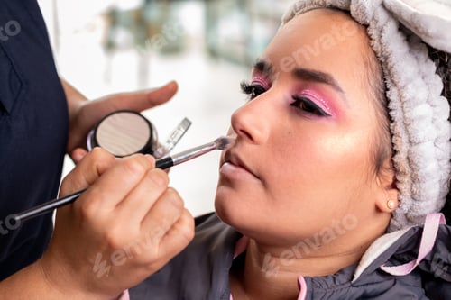 Preview: Professional makeup artist applying makeup to a latin woman's face with a makeup brush.