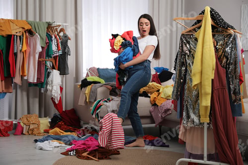 Preview: Upset young woman with lots of clothes in room. Fast fashion