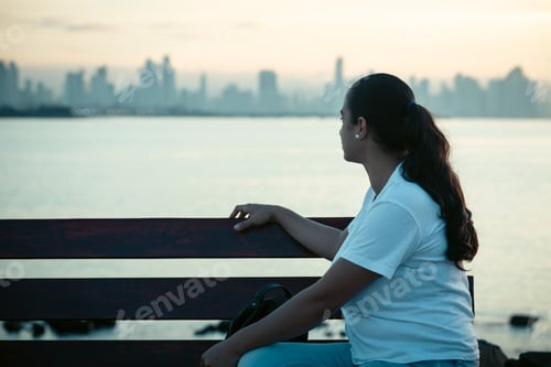 Preview: woman sitting on a bench thinking, while watching the sunrise