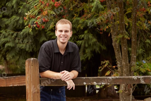 Preview: Young man leaning against wooden fence in forest