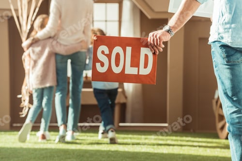 Preview: cropped shot of man holding sold signboard with young family moving into new cardbord house